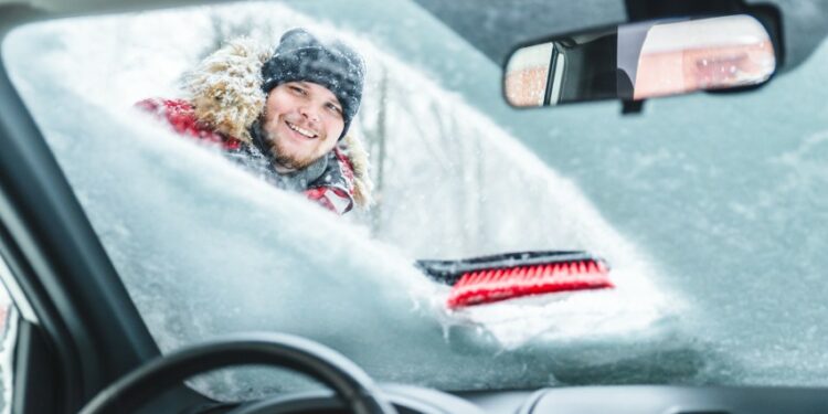 vyras valo priekini automobilio langa nuo sniego