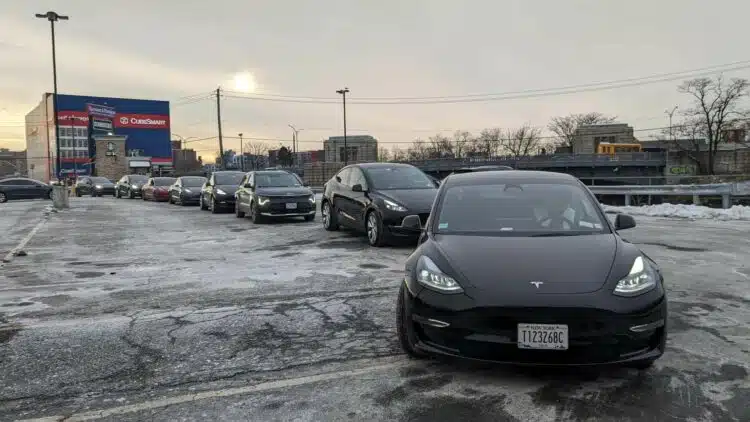 tesla elektromobiliai laukia eileje prie ikrovimo stoteliu