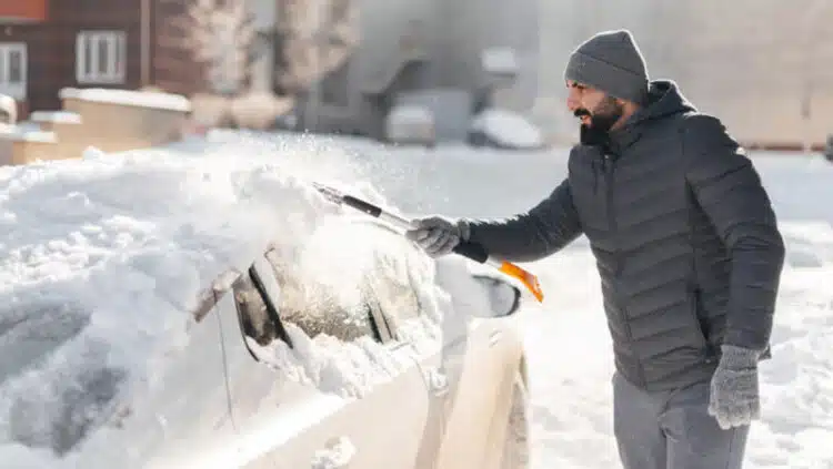vyras valo sniega nuo automobilio