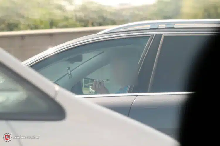 vairuotoja naudojasi mobiliuoju telefonu vairuodama automobili