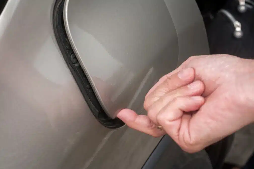 automobilio degalu bako dangtelis prispaustas pirstas