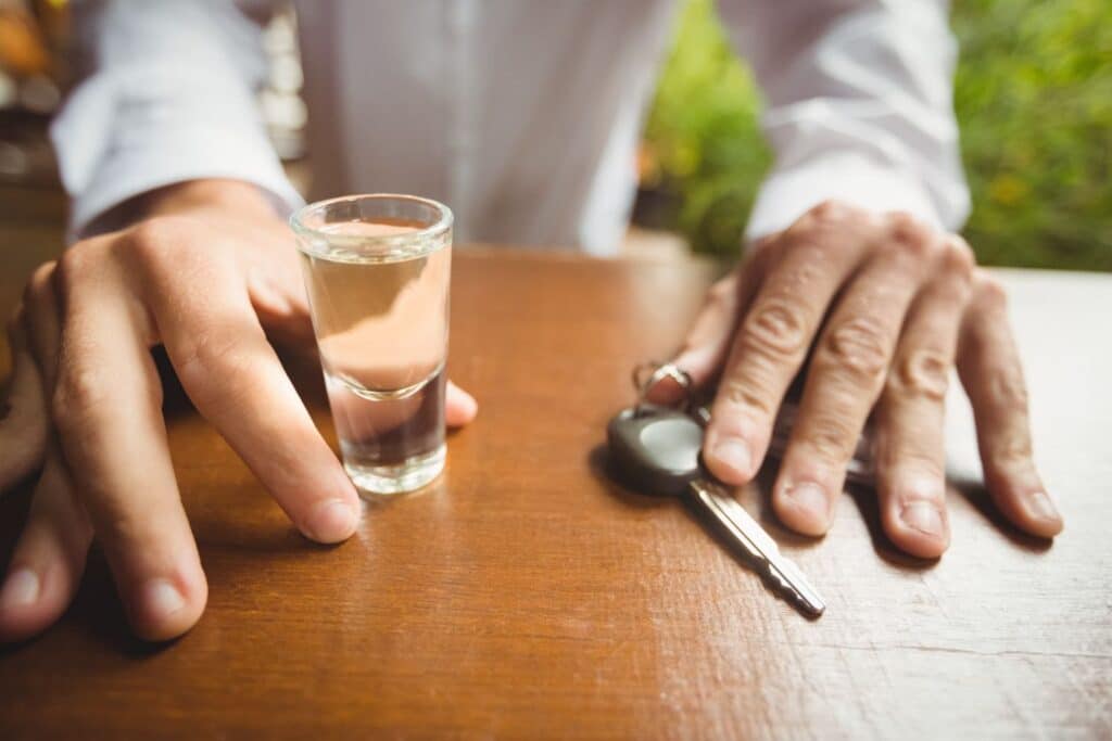 vyras sedi prie stalo su automobilio raktu ir alkoholiu