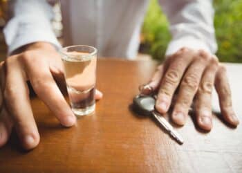 vyras sedi prie stalo su automobilio raktu ir alkoholiu