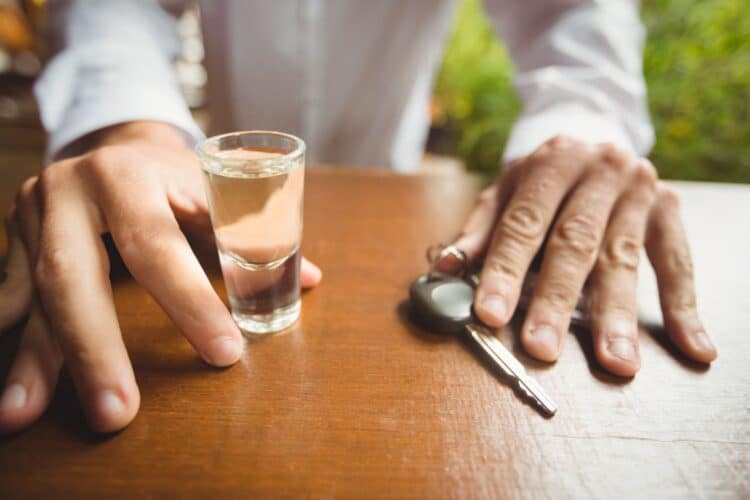 vyras sedi prie stalo su automobilio raktu ir alkoholiu