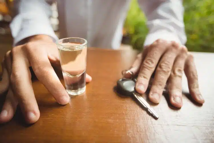 vyras sedi prie stalo su automobilio raktu ir alkoholiu