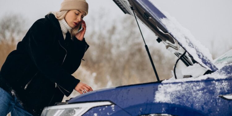 moteris kalba telefonu prie atidaryto automobilio variklio dangcio