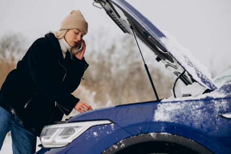 moteris kalba telefonu prie atidaryto automobilio variklio dangcio
