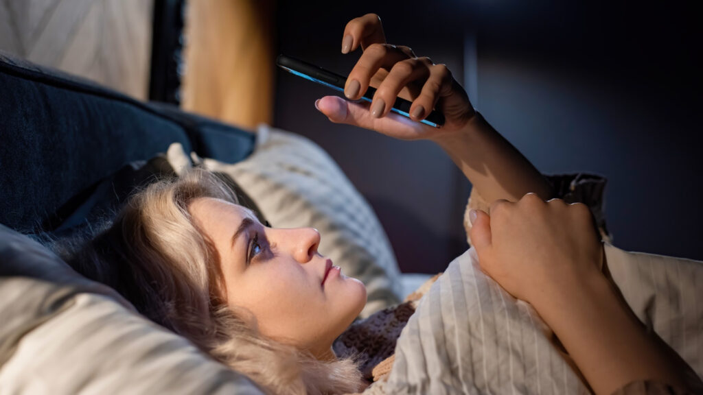 moteris ziuri i telefono ekrana pries miega lovoje