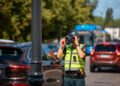 policijos pareigunas stebi eisma per ziuronus salia gatves vaziuojamosios kelio dalies