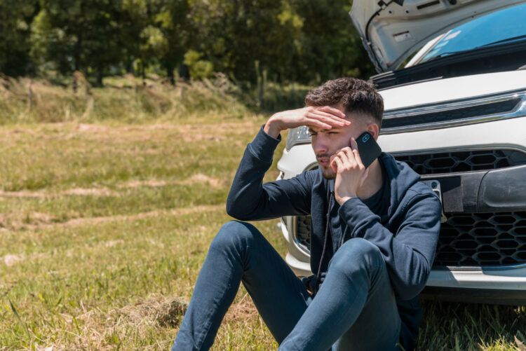 vyras sedi prie sugedusio automobilio