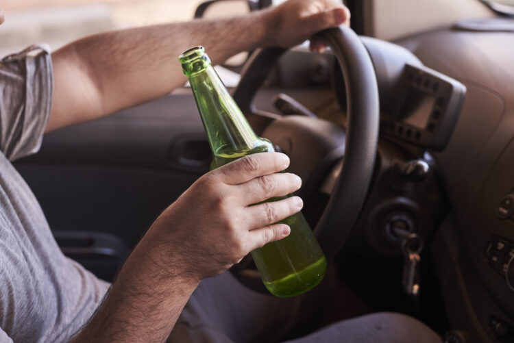 Alaus butelis vyro rankose vairuojant automobilį dienos metu