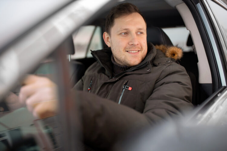 vyras sedi uz automobilio vairo su silta ziemine striuke