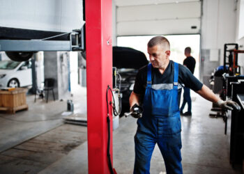 Automobilių remonto ir techninės priežiūros tema mechanikas uniformoje,dirbantis automobilių servise