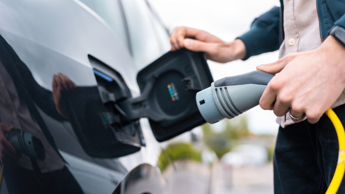 Vyras prijungiantis automobilio įkrovimo lizdą ir laikantis įkroviklį prie įkrovimo stotelės hibridinis automobilis ikraunamas phev