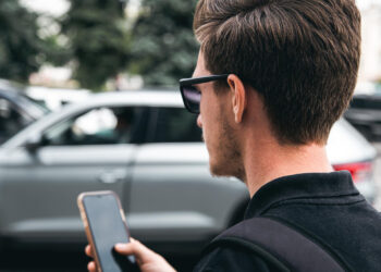 Jaunas vyras su akinais nuo saulės artimas planas kaip jis naudoja išmanųjį telefoną nuotrauka foto