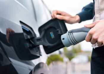 Vyras prijungiantis automobilio įkrovimo lizdą ir laikantis įkroviklį prie įkrovimo stotelės