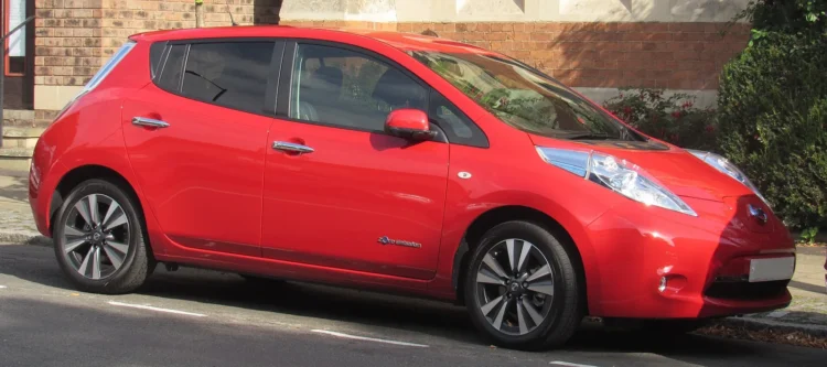 Pusmetį po baterijos keitimo seno „Nissan Leaf“ vairuotojas su viena įkrova nuvažiuoja per 400 km 1 Nissan Leaf baterijos keitimas: raudonas pirmosios kartos Leaf hečbekas su 30 kWh baterija stovi gatvėje