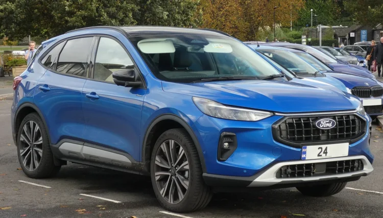 Nuo 2023 m. rugpjūčio pagaminto populiaraus krosoverio vairuotojai gali nežinoti, kad įspėjimai išjungti 1 Mėlynas atnaujintas Ford Kuga krosoveris stovi aikštelėje, matomas priekis ir šonas