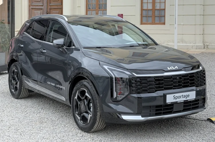 Naudotas Kia Sportage V: pilkas atnaujintas visureigis iš priekio ir šono, stovintis ant žvyro prie pastato