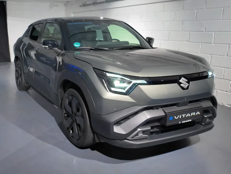 Japoniškos markės elektrinis krosoveris už 37 380 eurų – testuotojai įvardijo du trūkumus, svarbius ilgoje kelionėje 1 Suzuki e Vitara testas: pilkas elektrinis krosoveris iš priekio ir šono prie baltos plytų sienos