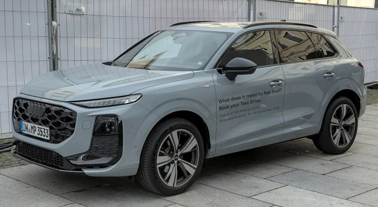 Įkraunamo vokiško krosoverio pirkėjams – bazinis hibridas neteko ketvirtadalio galios, kaina liko panaši 1 Pilkas naujos kartos Audi Q3 visureigis iš priekio ir šono, stovintis ant trinkelėmis grįstos aikštės