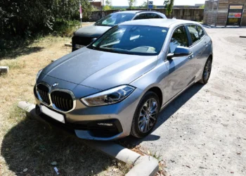 Naudota BMW 1 serija F40: pilkas hečbekas iš priekio ir šono, stovintis aikštelėje prie žolės