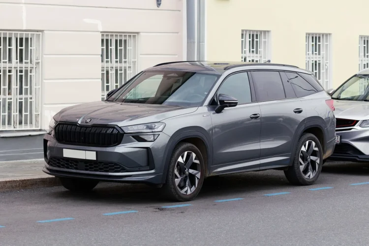 Pilka antrosios kartos Škoda Kodiaq iš priekio ir šono, stovinti gatvėje prie pastato