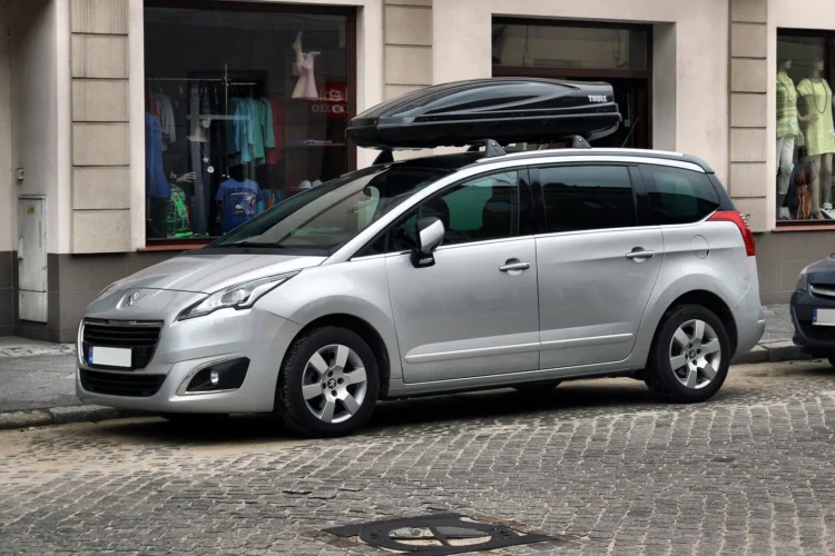 Keturios naudoto „Peugeot 5008“ benzininės versijos, kurių geriau vengti, ir vienas patikimesnis dyzelis 1 Sidabrinis atnaujintas pirmosios kartos Peugeot 5008 su bagažo dėže ant stogo, stovintis grįstoje gatvėje