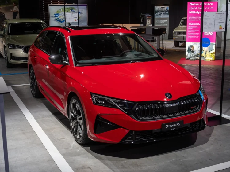Hibridinės Octavia kaina: raudonas atnaujintas Škoda Octavia Combi universalas iš priekio ir šono parodos stende
