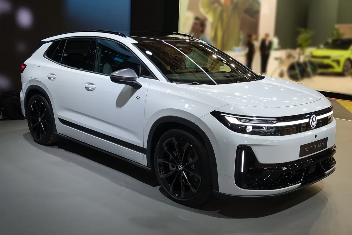 Šeimai elektrinio visureigio ieškantiems – retas atvejis, kai „Volkswagen“ 1 220 eurų pigesnis už „Škoda“ 1 ID. Tiguan kaina: baltas elektrinis Volkswagen ID. Tiguan visureigis iš priekio ir šono parodoje