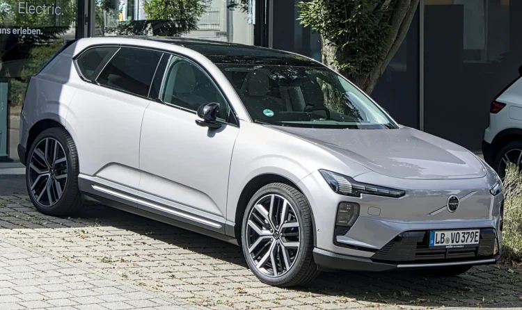 Jei naują elektrinį švedų visureigį krausite tik greitose stotelėse – neteksite pigių kilometrų 1 Volvo EX60 sąnaudos: sidabrinis elektrinis visureigis Volvo EX60 iš priekio ir šono ant grįstos aikštelės